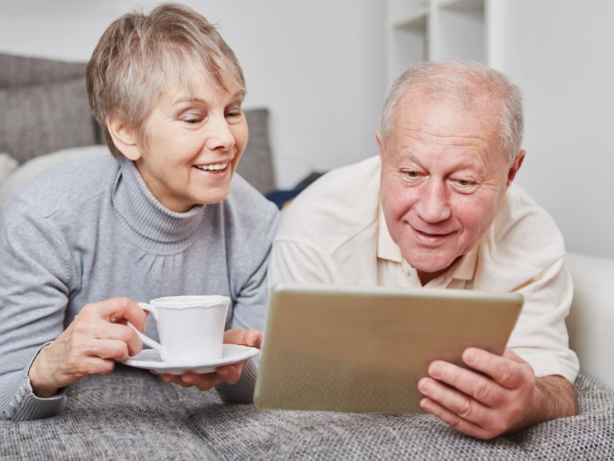 White-haired man and women smiling while looking at computer tablet
